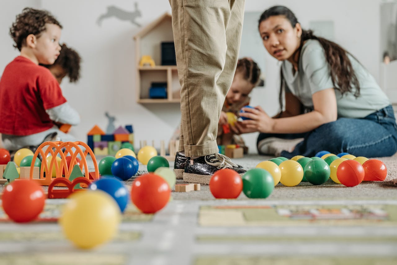 Children and a teacher playing with toys in a kindergarten setting indoors.